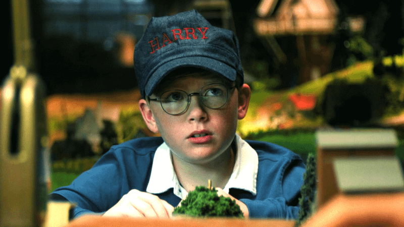 Jude Hill as Harry Vandergroot wearing a train engineer cap and sitting at a model town in Holland